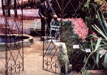 Statue of a man, a little boy, and a dog in a garden lined with pink flowers